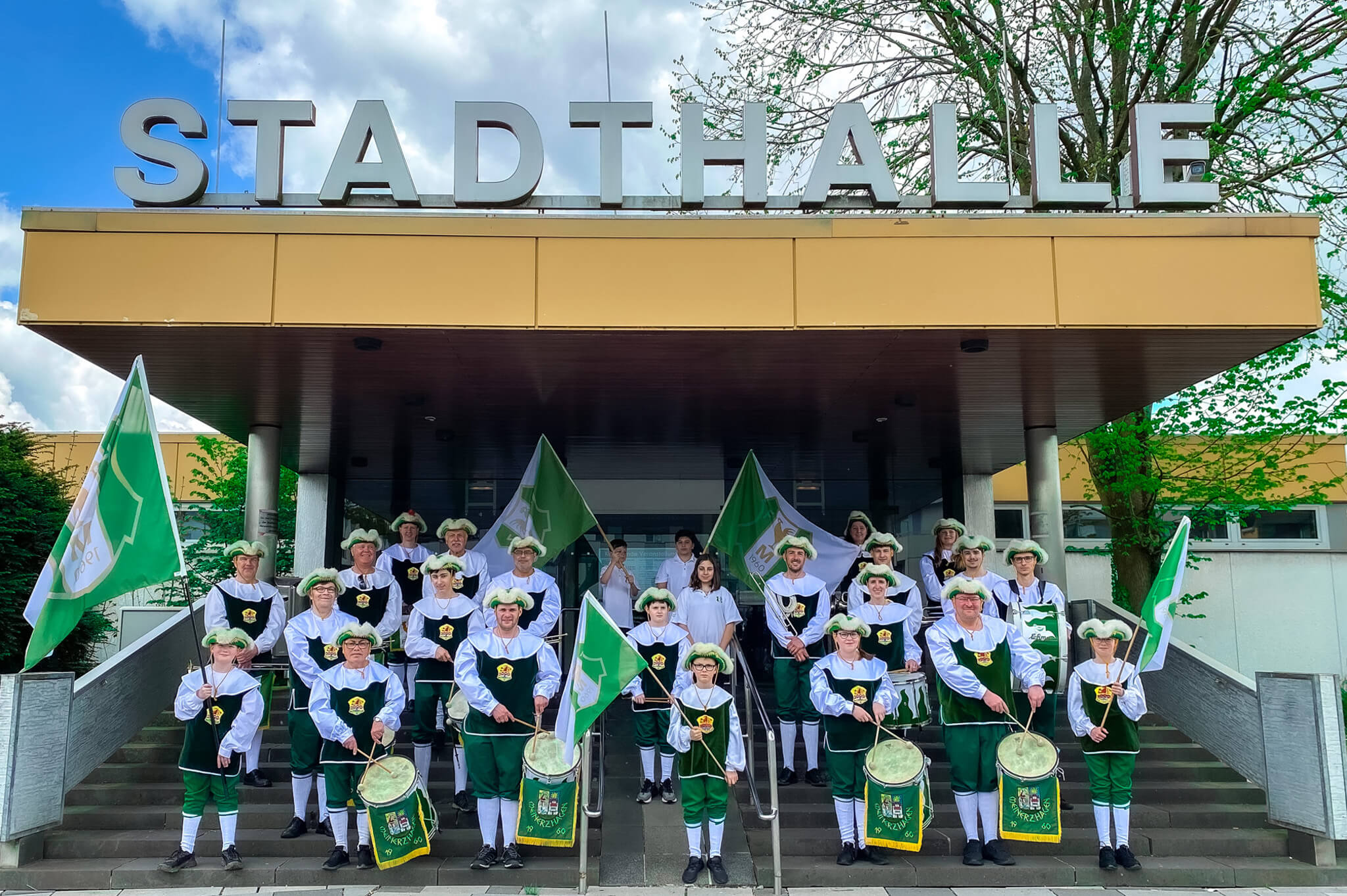 Titelbild- Kompletter-Fanfarenzug-an-der-Stadthalle-und-hält-die-Flaggen-hoch
